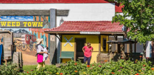 Two women stand in front of a play rail road station watching their children.