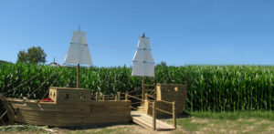 A giant wood ship with white sails sits at the entrance of a corn maze.