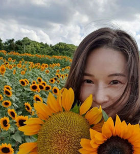 Portrait of a young woman in a flower field with sunflowers covering part of her face